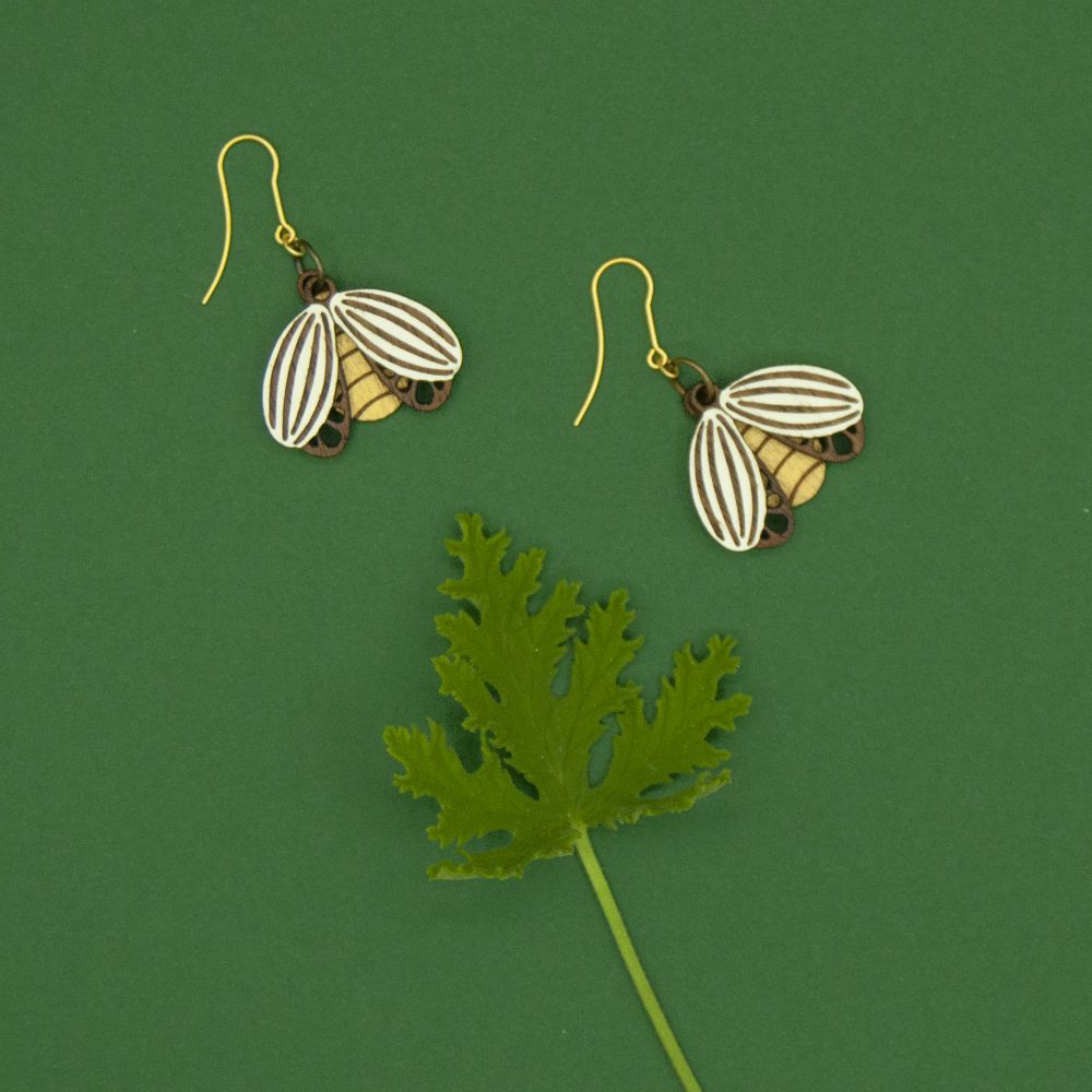 Woodcut beetle earrings set against a green background.