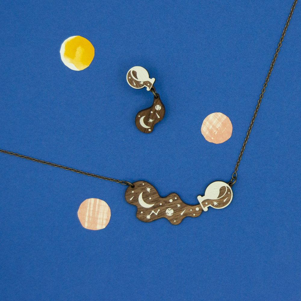 Drip Earrings and matching Spill Necklace are styled against a blue background.