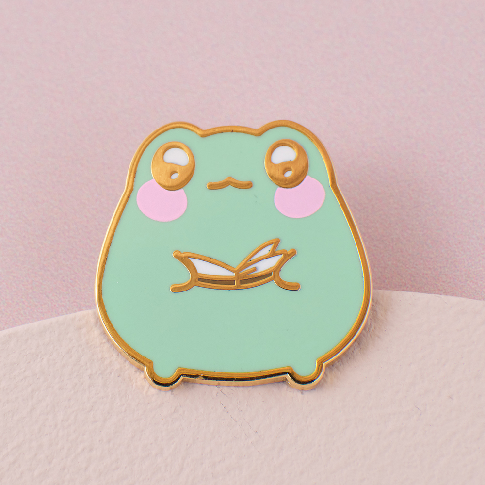 enamel pin of lily the frog reading a book