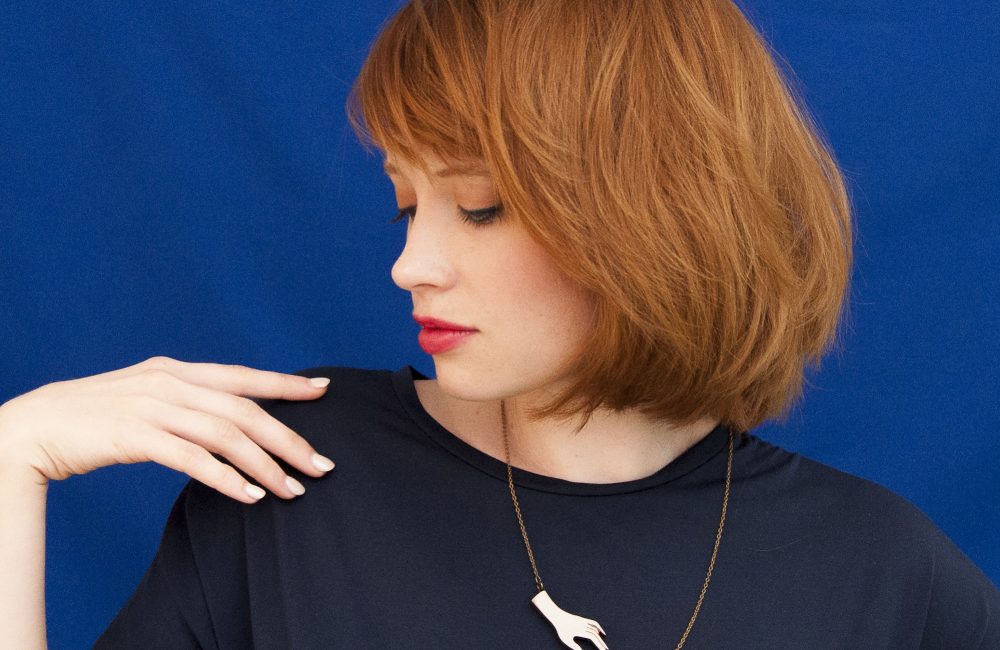 A female model wears a lasercut necklace against a blue background.
