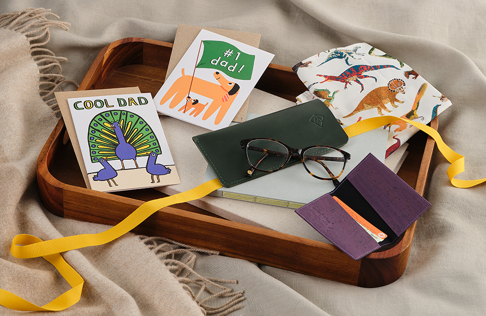 lifestyle image of a wooden tray on a bed, filled with father's day cards and presents