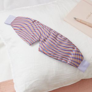 A sleepmask in a purple and pink wavy pattern, lain across a pillow.