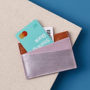A leather card holder with two slots on the front. The first panel is metallic lilac, the middle one is a matte lilac, and the back panel is a grainy tan.