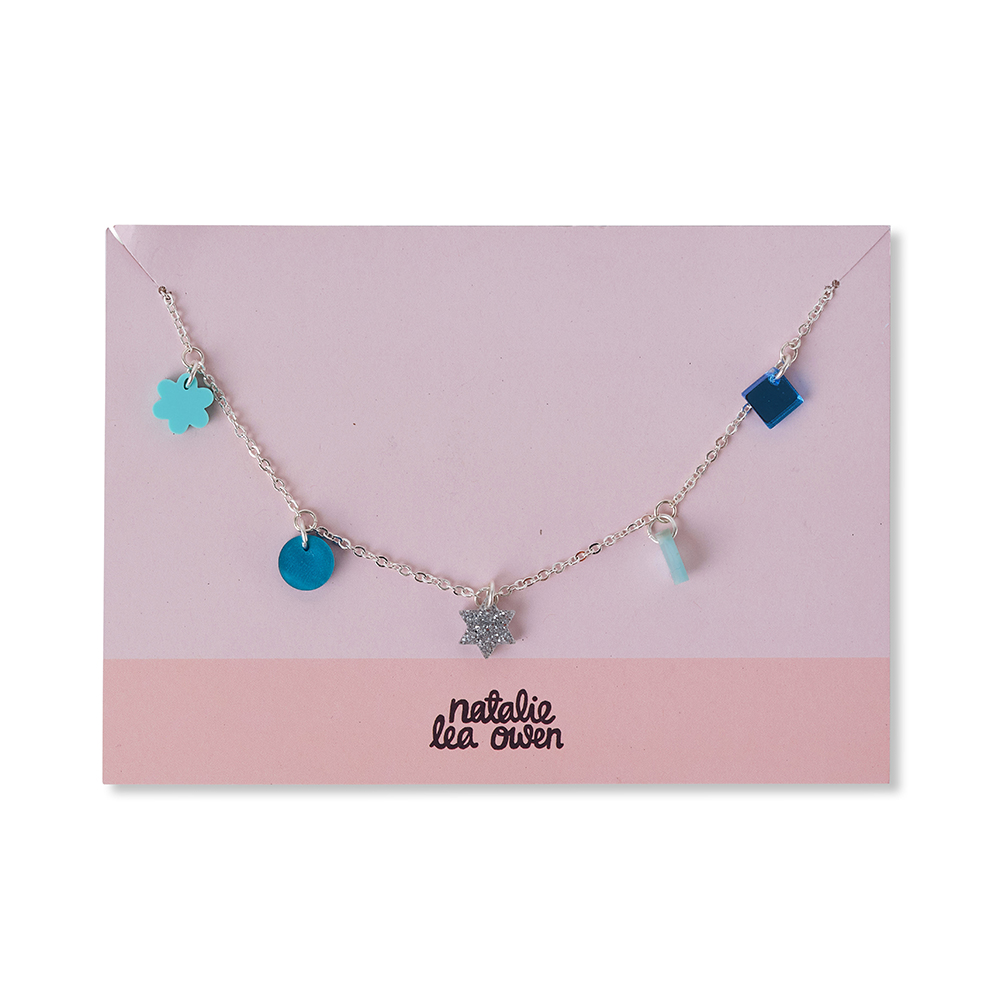 Silver charm necklace by jewellery designer Natalie Lea Owen. Blue and green, small charms in abstract shapes. The necklace is presented on a branded pink card.