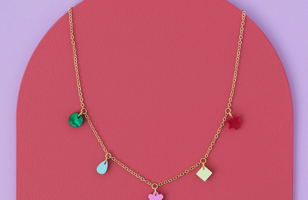 Silver chain multi-coloured charm necklace on a pink and lilac background.