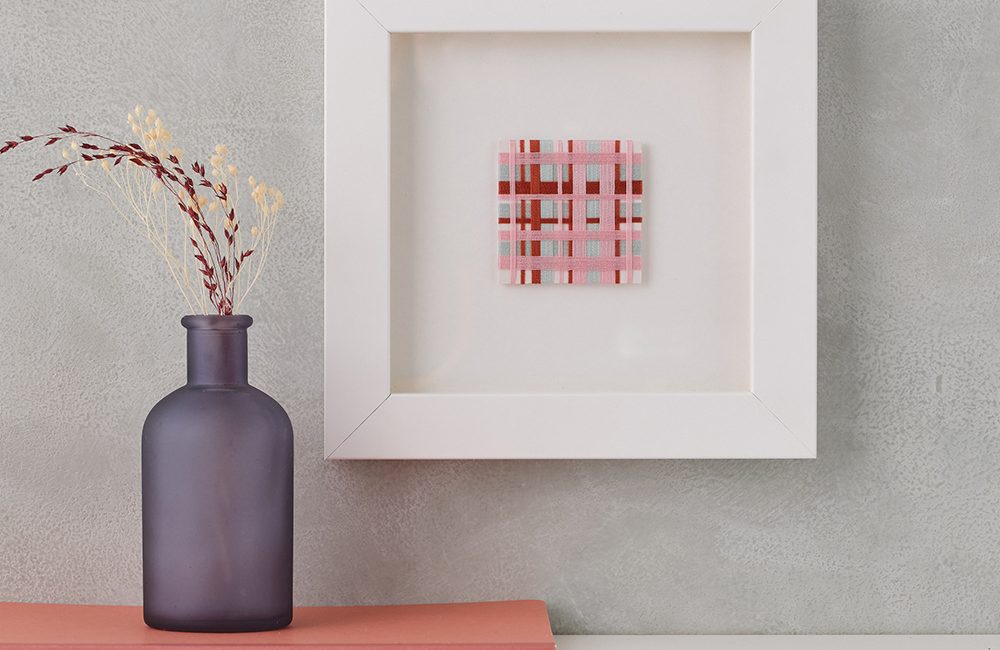 Colourful Journey I Framed Artwork Woven pink, red and blue small square artwork. Mounted on grey wall.