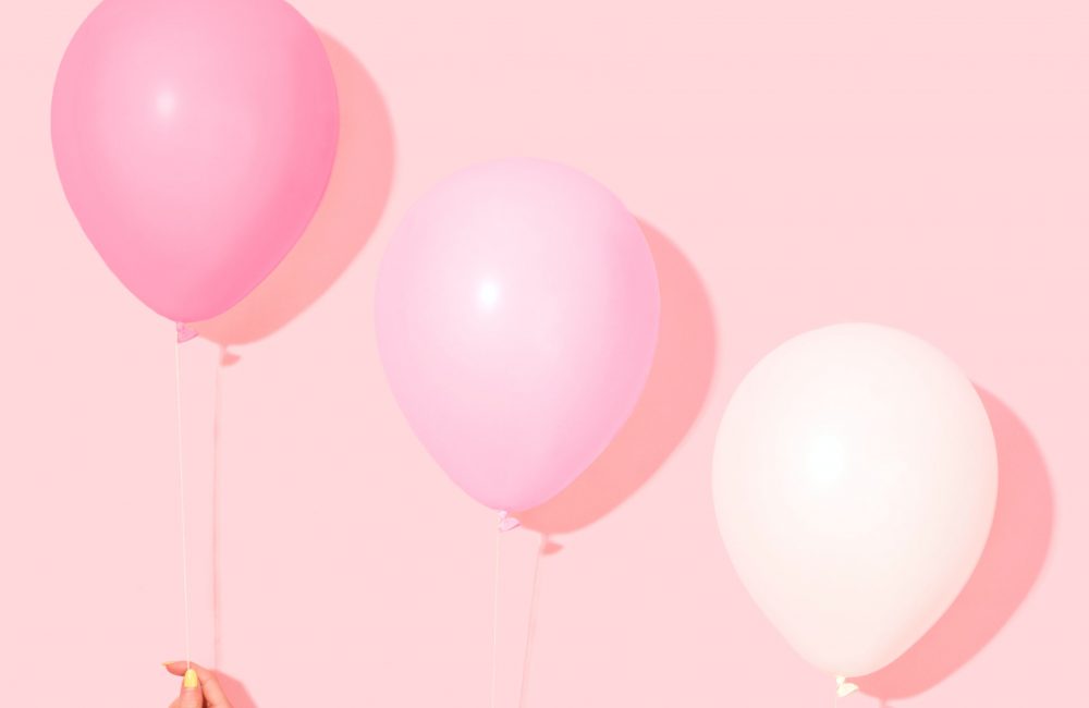 Three hands holding pink balloons