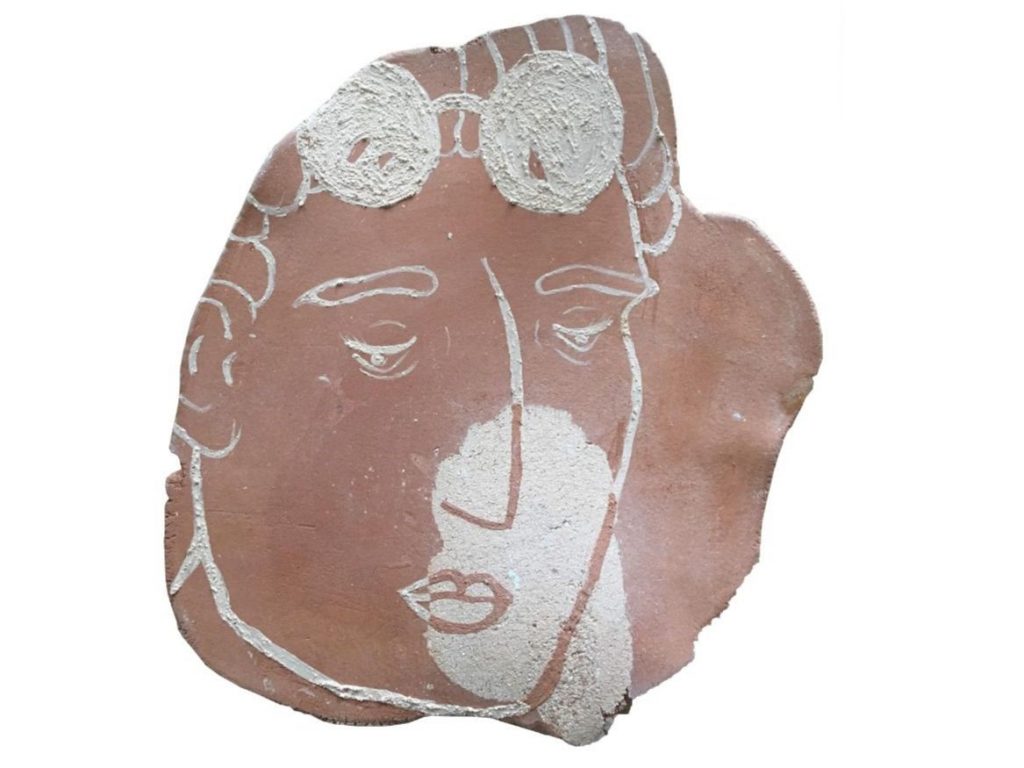 A terracotta piece of clay with an illustrated face on